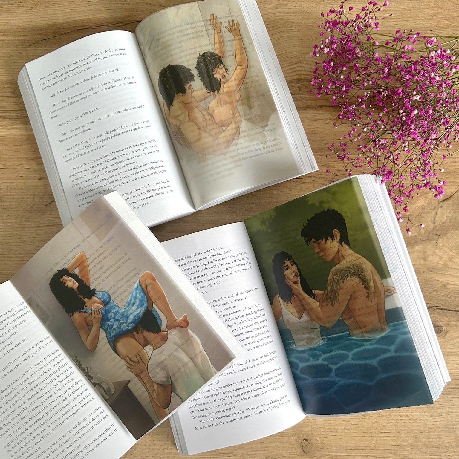 Open books with illustrations of people on a wooden surface with pink flowers.